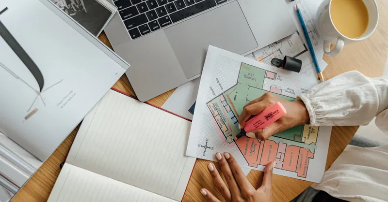 Top view of an architect working on floor plans with a laptop and coffee, highlighting remote work creativity.