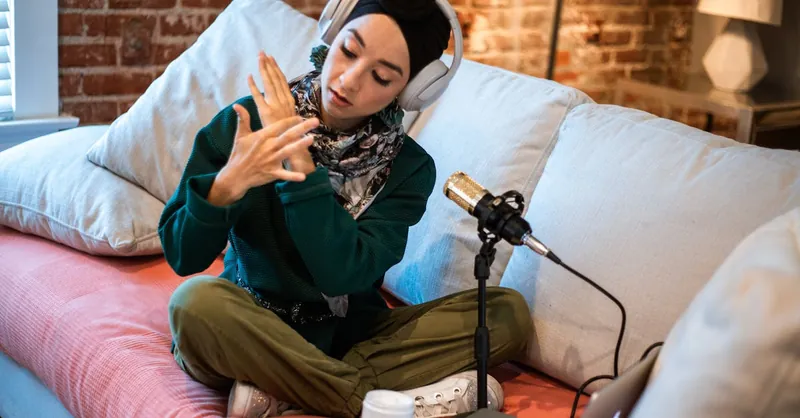 Woman podcasting at home, wearing headphones and using a microphone, creating content.