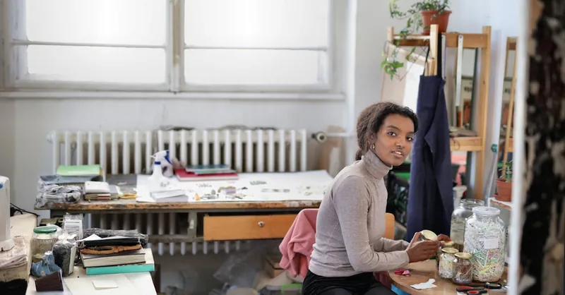 A woman in a creative workspace surrounded by art supplies and plants, exuding creativity and focus.