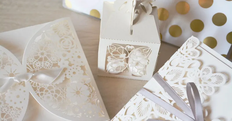 Beautiful laser cut invitations and gift box with intricate designs and ribbons, perfect for weddings or special events.