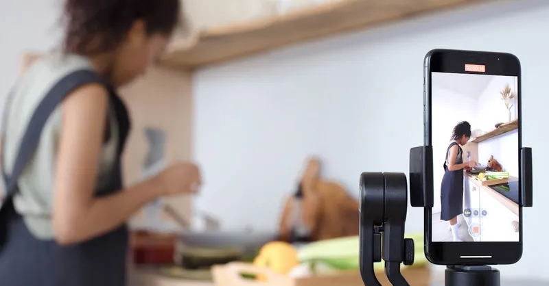 Woman using smartphone to record a cooking tutorial in a modern kitchen setting.