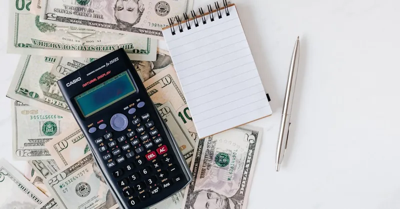 Flat lay of US dollar bills with calculator and notebook for budgeting.
