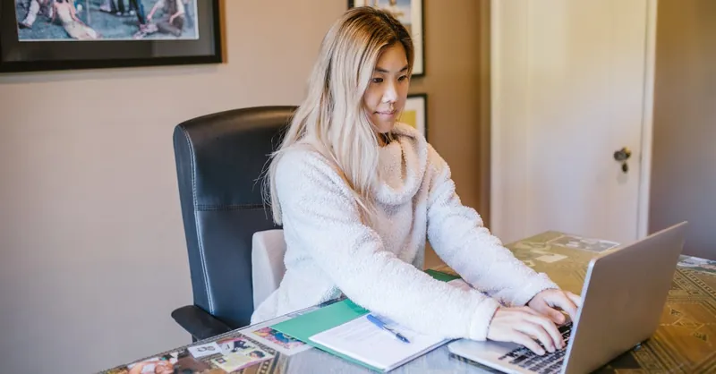 Young woman working remotely on laptop from home office, representing modern remote work lifestyle.