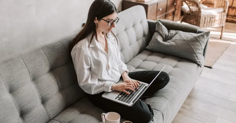 Woman in a cozy home setting working on a laptop for remote work and relaxation.