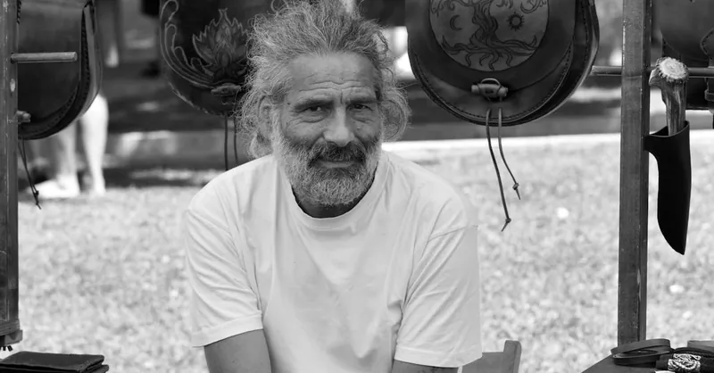 Portrait of an artisan vendor at an outdoor market in Italy, showcasing handmade leather crafts.