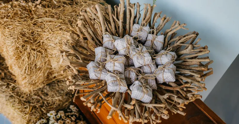 A rustic and artistic display of handmade gifts in a wooden bowl with hay and chamomile accents.