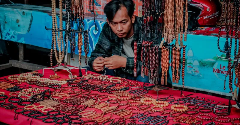 Man selling handmade beaded bracelets and necklaces at a vibrant urban market stall.