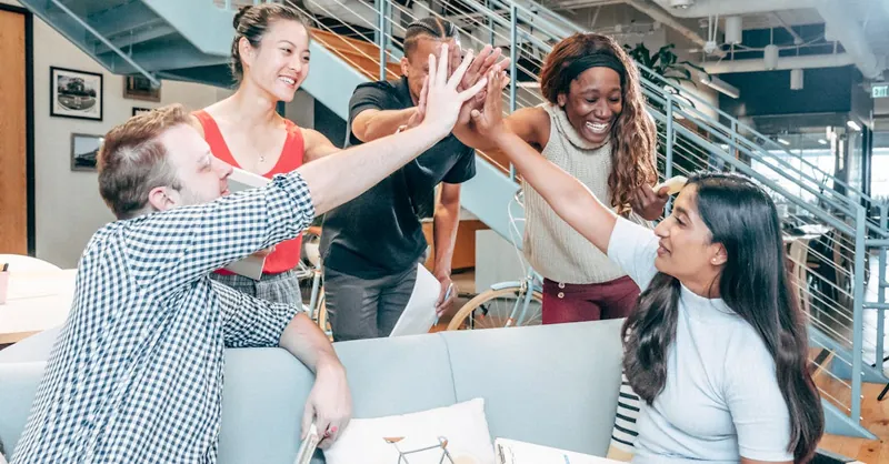 A diverse team celebrates success with a high-five in a modern office setting.