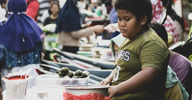 Young boy working at a busy street market, engaging with customers.