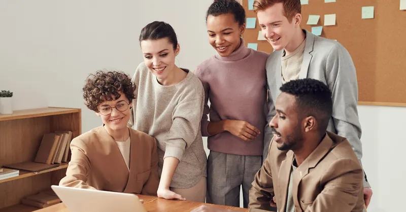 Group of diverse professionals engaged in brainstorming session around a laptop indoors.