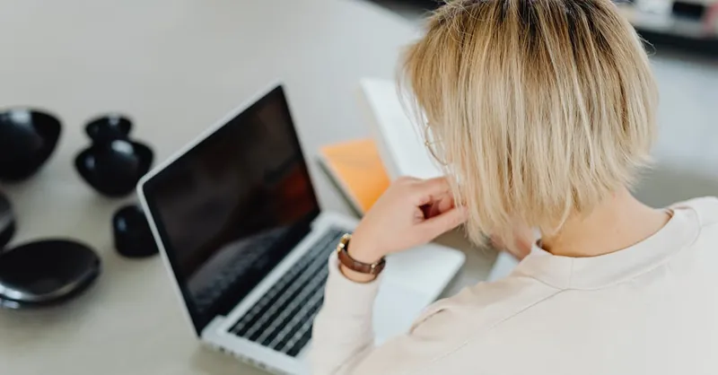 A woman with short blond hair working on a laptop at home.