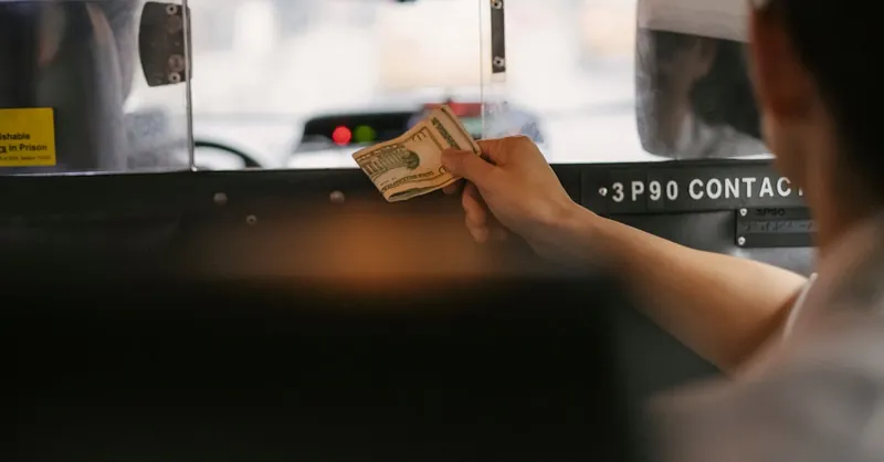 Closeup of a person handing cash to a taxi driver through the partition during a ride in a busy city.
