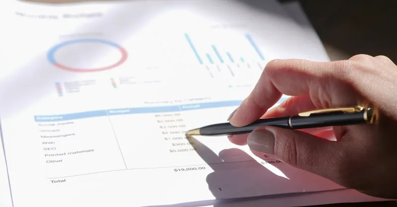Hand holding pen, analyzing budget with charts and graph paper.