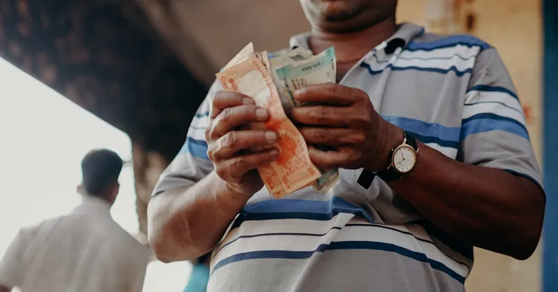 Man in Indian market counting rupee notes, showcasing daily street commerce.