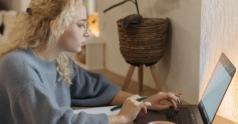 Young woman focused on remote work in a cozy indoor setting with a laptop and coffee cup.
