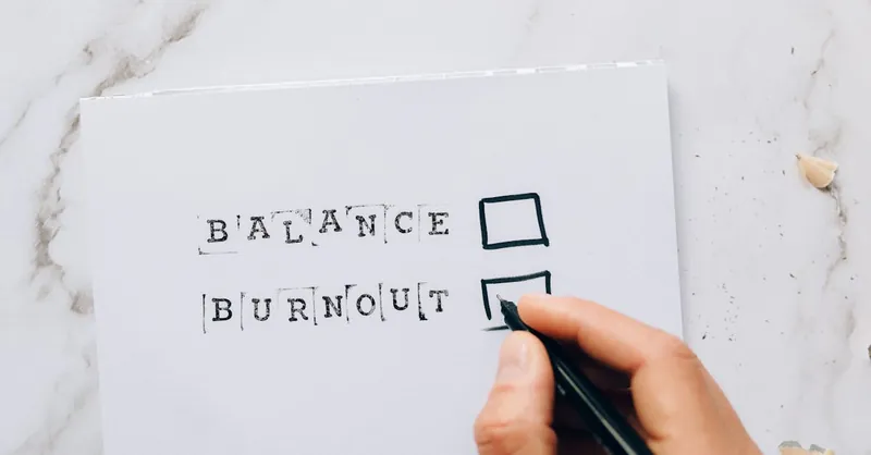Close-up of a hand hovering over a checklist with options for balance or burnout, symbolizing stress and choice.