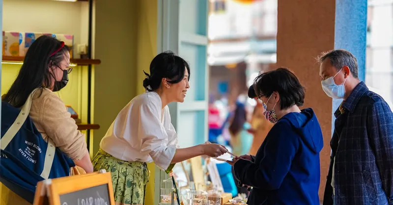 A vendor engaging with customers at a Taipei market, showcasing handmade crafts and jewelry.