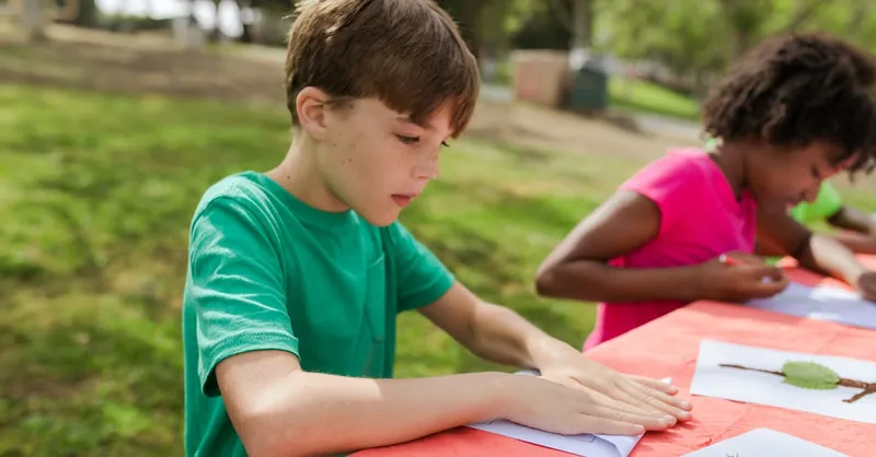 Young kids engage in outdoor crafting activities during summer camp, learning and having fun.