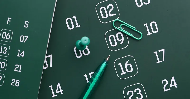 Close-up of a green calendar with pen, push pin, and paper clip for planning and organization.
