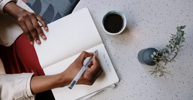 Person writing in a planner with coffee at a café, focusing on planning and productivity.