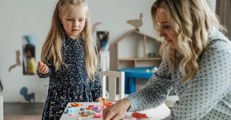 A young girl and a woman engage in a creative activity at a preschool classroom, fostering learning.